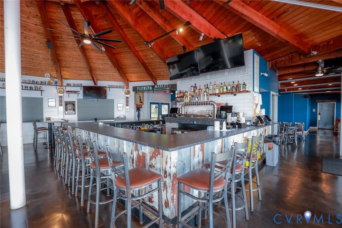 700 Jordan Point Road, North Prince George, VA 23860 Bar area featuring a vaulted wood-plank ceiling with exposed beams, a multi-tiered stone-topped bar, corrugated metal paneling, white subway tile backsplash, and polished concrete flooring