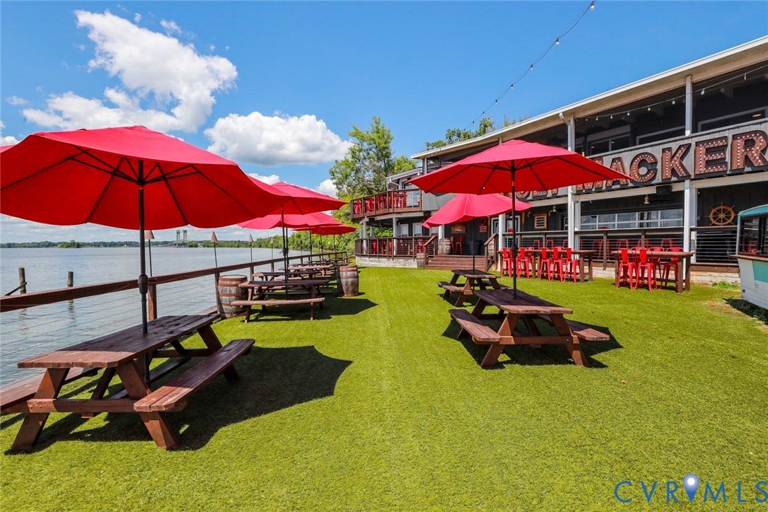 700 Jordan Point Road, North Prince George, VA 23860 Waterfront outdoor space featuring an expansive artificial turf lawn, a perimeter wood railing, and an elevated building exterior with integrated string lighting