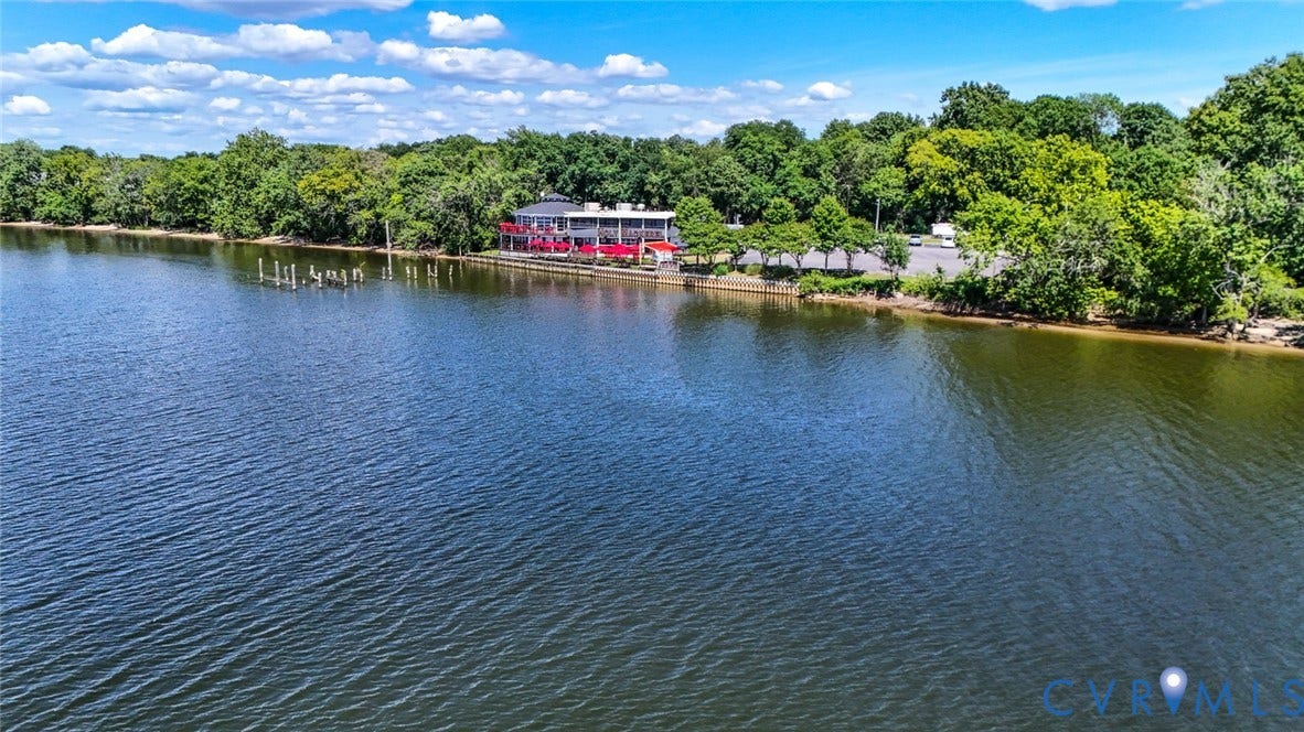 700 Jordan Point Road, North Prince George, VA 23860 Waterfront property featuring a multi-level structure, paved parking area, wooden dock pilings, and expansive natural shoreline