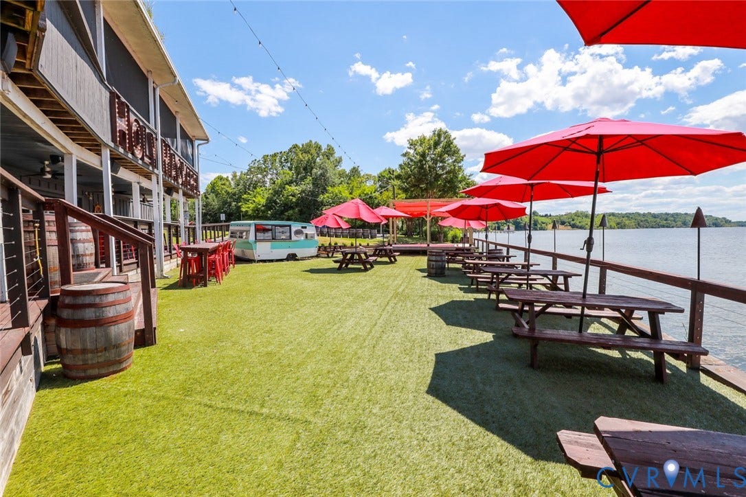 700 Jordan Point Road, North Prince George, VA 23860 Extensive waterfront patio featuring synthetic turf, overhead string lighting, a wooden perimeter railing, and a multi-level deck structure