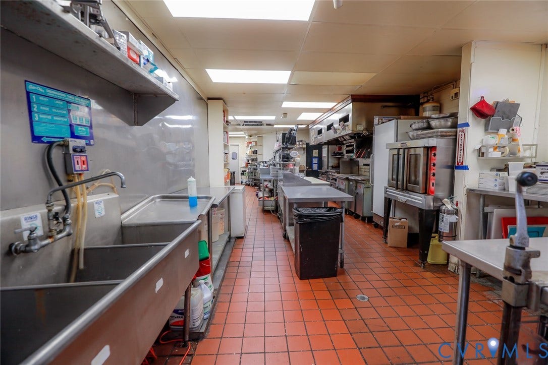 700 Jordan Point Road, North Prince George, VA 23860 Commercial kitchen featuring stainless steel wall-mounted shelving, triple-basin metal sink, industrial-grade tile flooring, and integrated stainless steel convection ovens