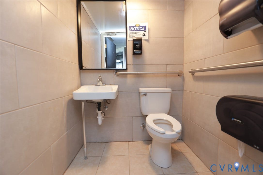 700 Jordan Point Road, North Prince George, VA 23860 Restroom featuring large-format wall tiling, wall-mounted sink with metal support, mirror with black frame, and installed safety grab bars