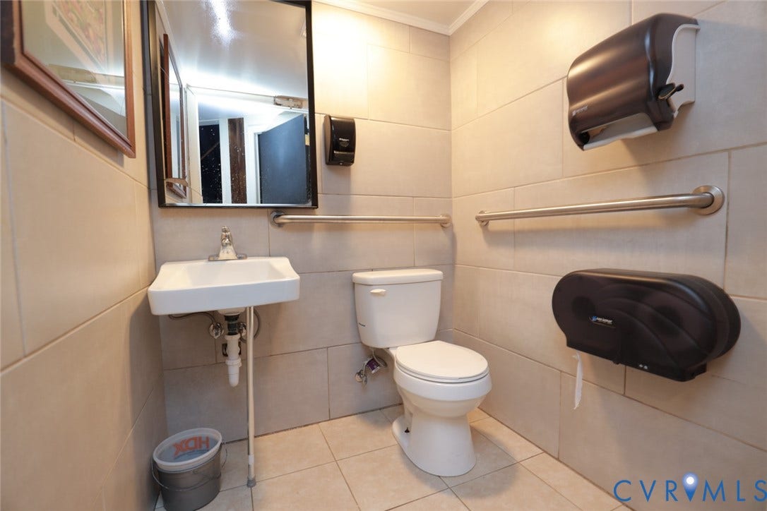 700 Jordan Point Road, North Prince George, VA 23860 Neutral-toned wall and floor tiling, wall-mounted sink, rectangular vanity mirror, and installed horizontal grab bars