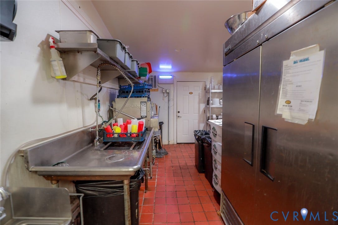 700 Jordan Point Road, North Prince George, VA 23860 Commercial kitchen prep area featuring stainless steel dual-basin sink, overhead shelving, industrial-grade stainless steel refrigeration unit, and durable quarry tile flooring