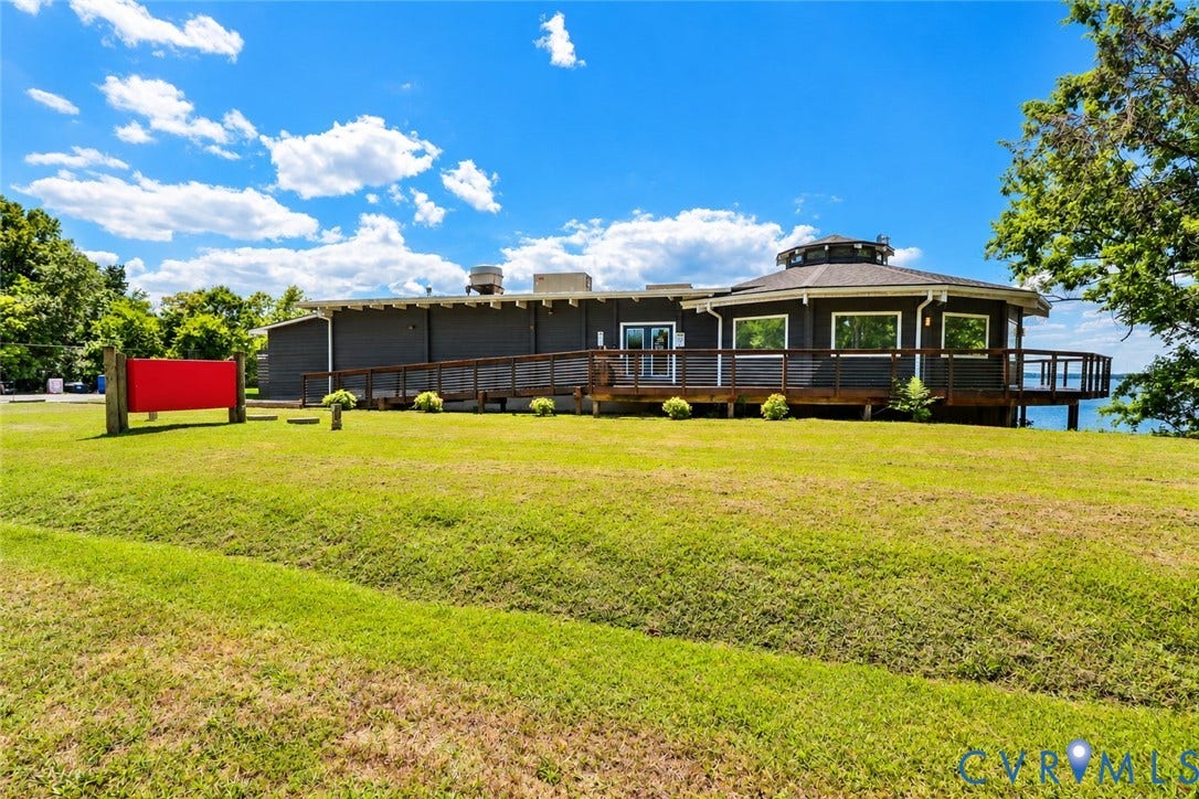 700 Jordan Point Road, North Prince George, VA 23860 Exterior featuring dark horizontal siding, a rounded roofline, an expansive wraparound deck with railing, and a sloped lawn