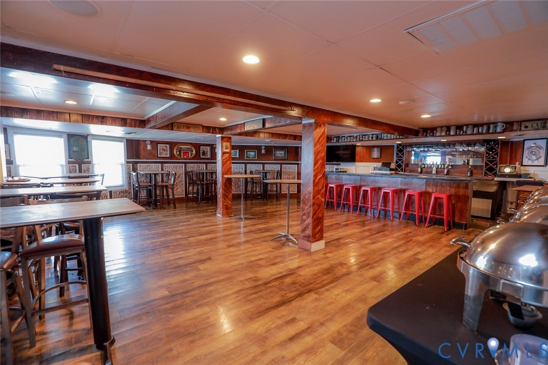 700 Jordan Point Road, North Prince George, VA 23860 Spacious interior featuring wood-finish flooring, built-in bar with mirror backing, recessed ceiling lighting, and decorative wood-wrapped support pillars