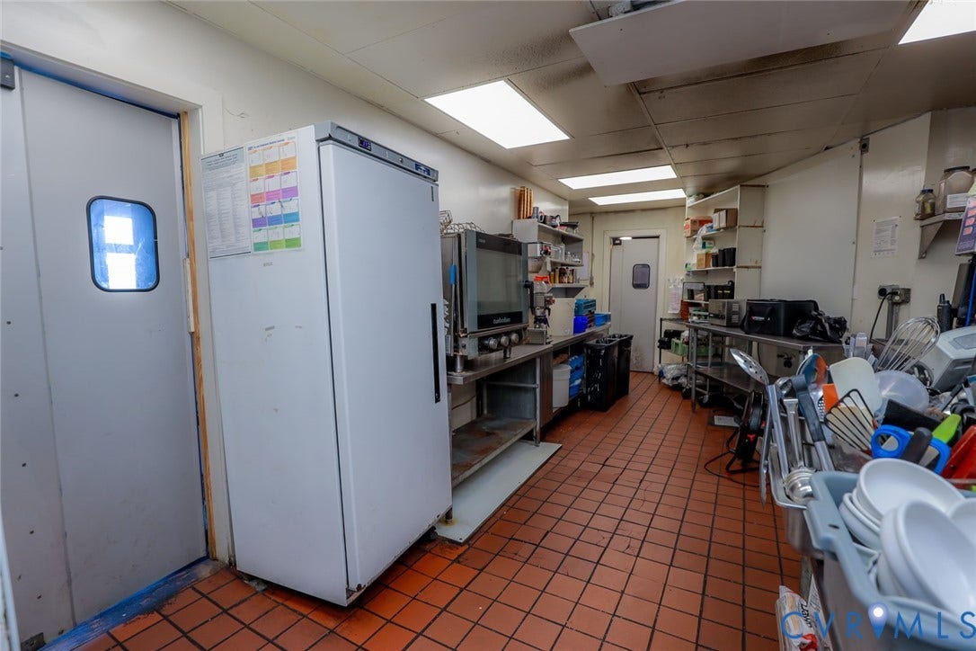 700 Jordan Point Road, North Prince George, VA 23860 Commercial kitchen workspace featuring durable tile flooring, recessed panel lighting, stainless steel work surfaces, wall-mounted shelving, and a full-height refrigerator