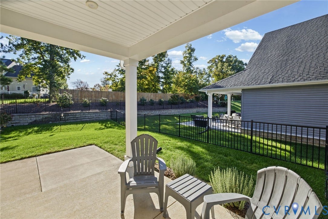 6525 Liddy Circle, Glen Allen, VA 23060 Covered concrete patio with a beadboard ceiling, manicured lawn, black metal perimeter fencing, and stone retaining wall