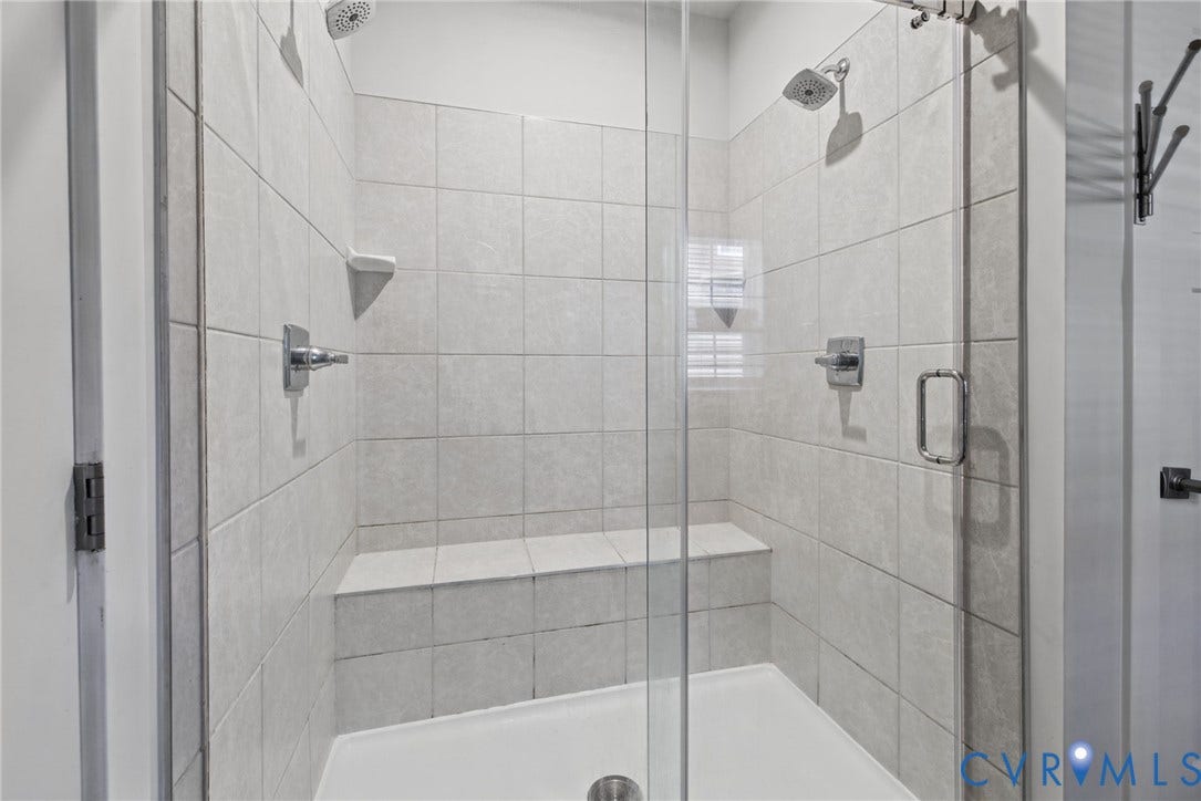 6525 Liddy Circle, Glen Allen, VA 23060 Walk-in shower featuring light-toned tile surround, built-in tiled bench, dual overhead showerheads, and upgraded frameless glass door.