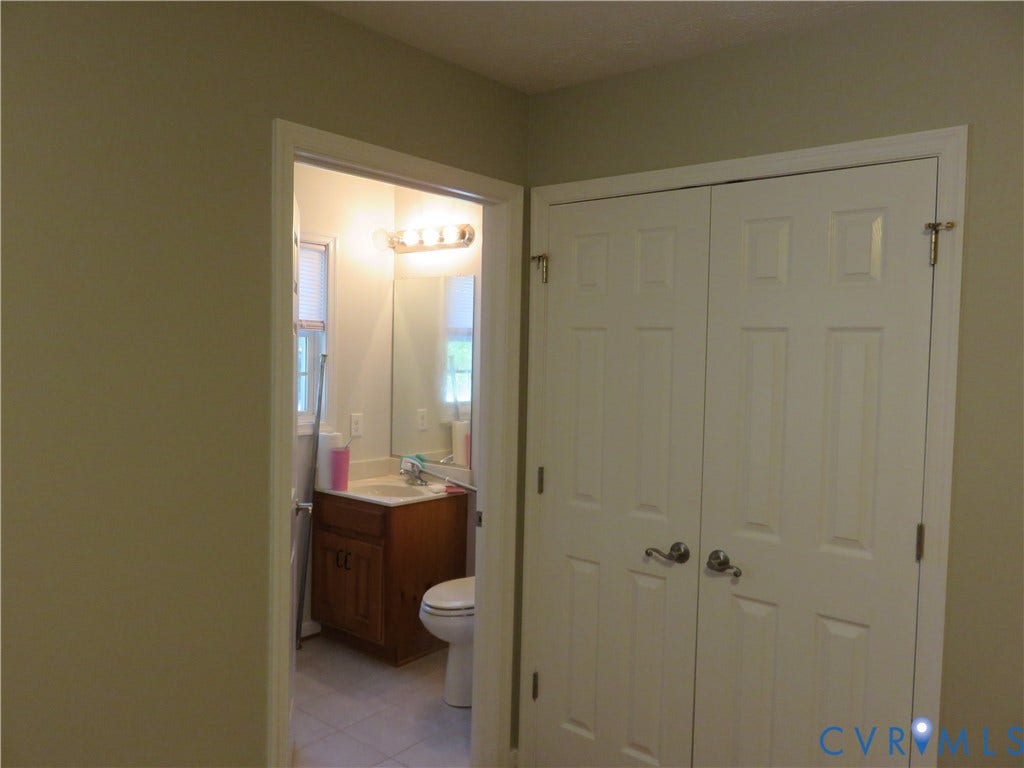 14 N Kalmia Avenue, Henrico, VA 23075 Six-panel white closet doors and interior bathroom featuring a wood-finish vanity, wall-mounted mirror, and multi-bulb light fixture