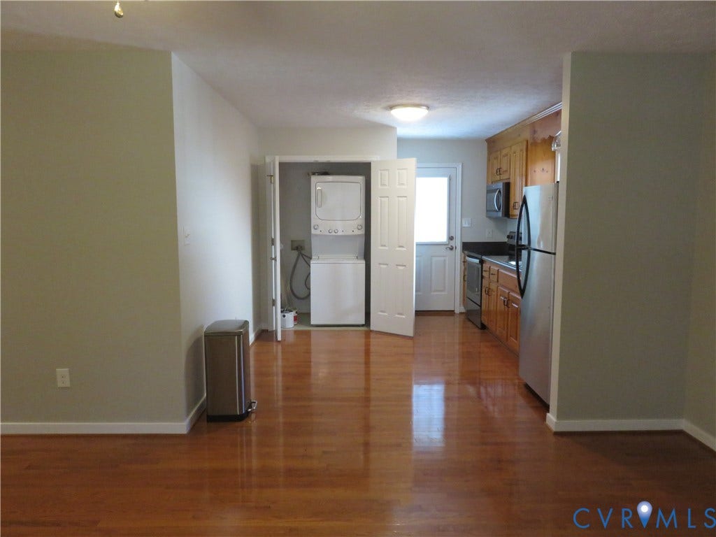 14 N Kalmia Avenue, Henrico, VA 23075 Kitchen featuring wood cabinetry, stainless steel appliances, and integrated laundry closet with stackable washer and dryer, complemented by wood-finish flooring