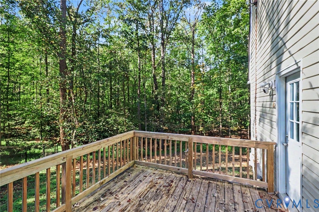 2511 Mill Road, Powhatan, VA 23139 Elevated wood deck with a simple railing, light-colored vinyl siding, and exterior entry door, set against a backdrop of mature trees