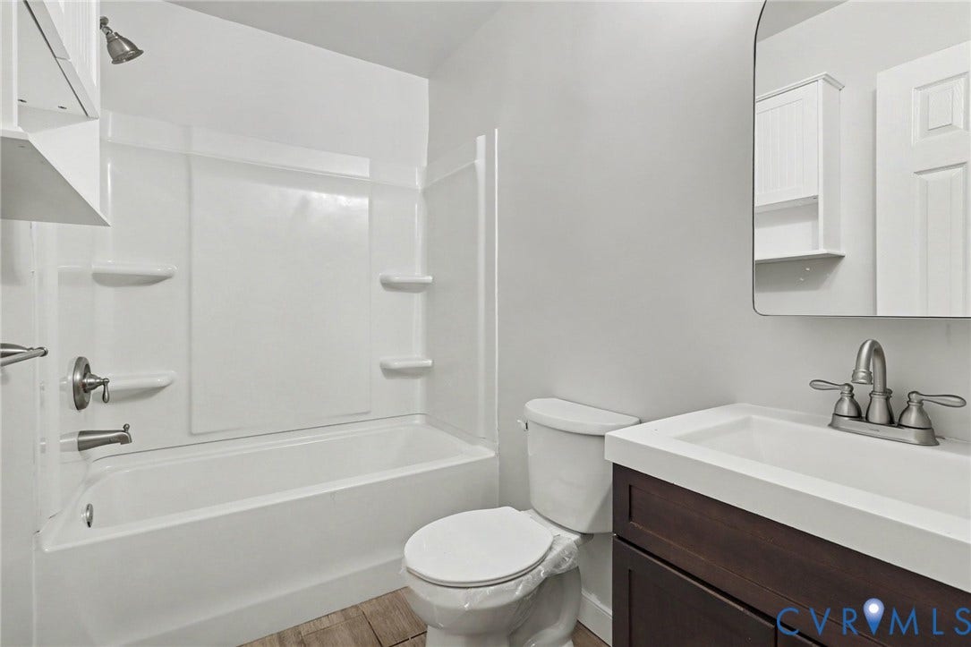 2511 Mill Road, Powhatan, VA 23139 Bathroom featuring a dark wood-finish vanity with a rectangular integrated sink, brushed nickel faucet hardware, tub-shower combination with built-in shelving, and an arched wall mirror