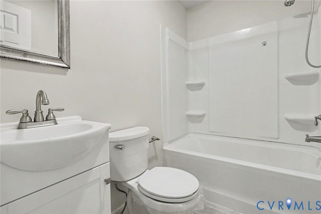 2511 Mill Road, Powhatan, VA 23139 Bathroom featuring a white vanity cabinet with a integrated sink, dual-handle faucet, elongated toilet, and a combined tub and shower unit with built-in shelving