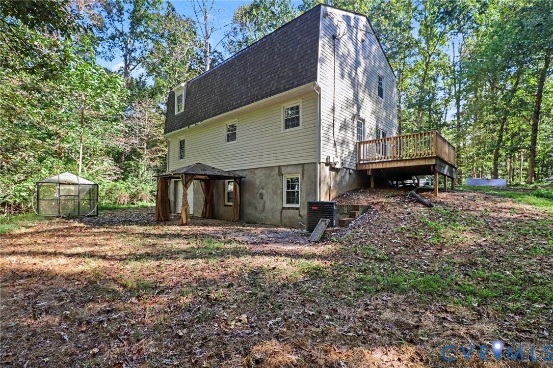 2511 Mill Road, Powhatan, VA 23139 Multi-story residence featuring light-toned vinyl siding, a shingled gambrel roof, an elevated wood deck, and a ground-level covered patio area set within a wooded lot