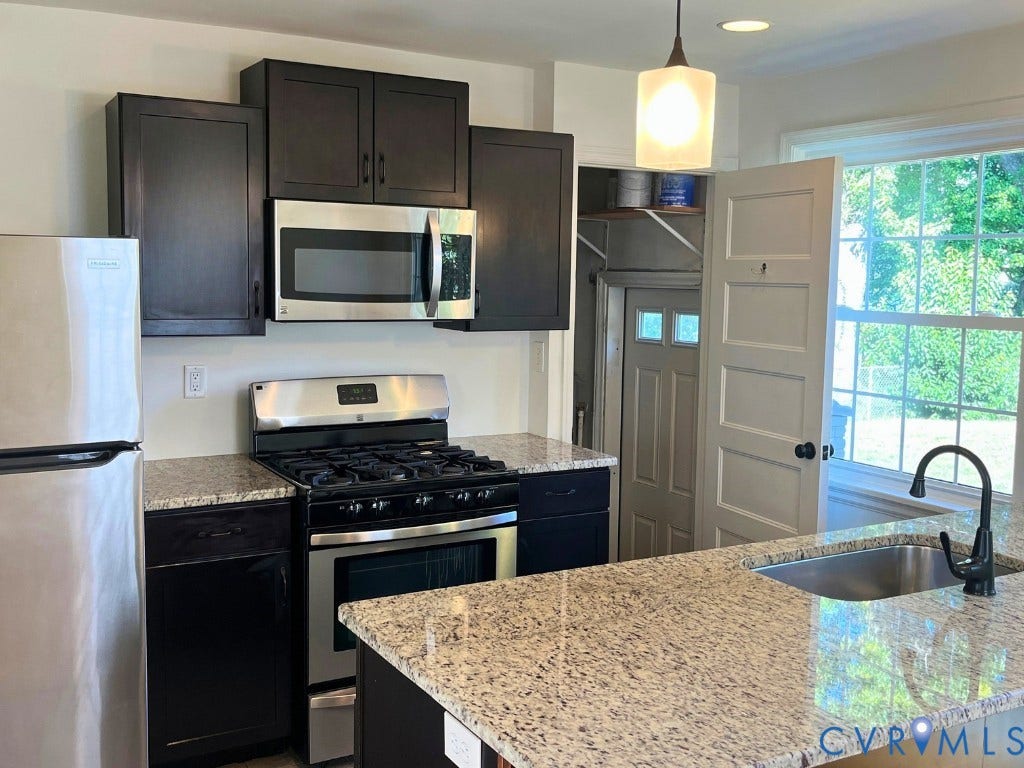 Kitchen featuring espresso cabinetry, stone-surface countertops, stainless steel gas range, microwave, and an undermount sink with a matte black faucet