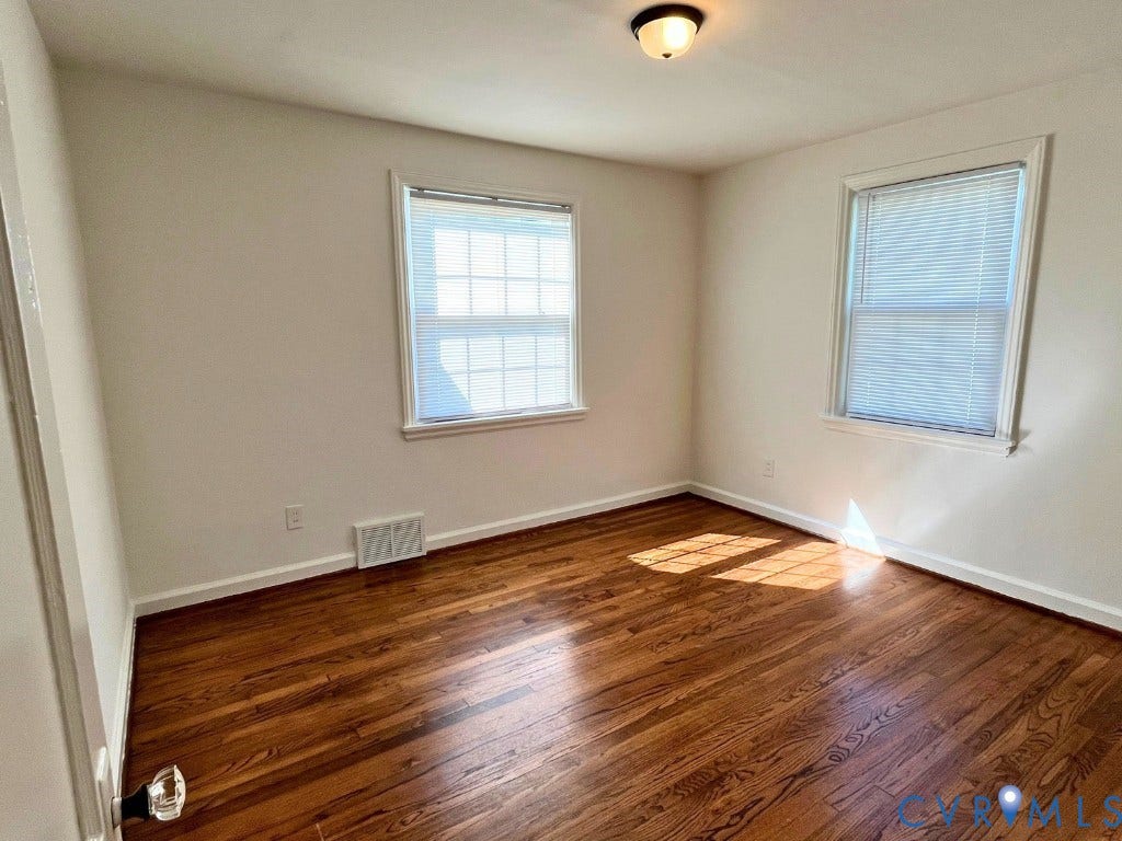 Room featuring wood-finish flooring, neutral wall paint, two windows with grid patterns, and a ceiling-mounted light fixture