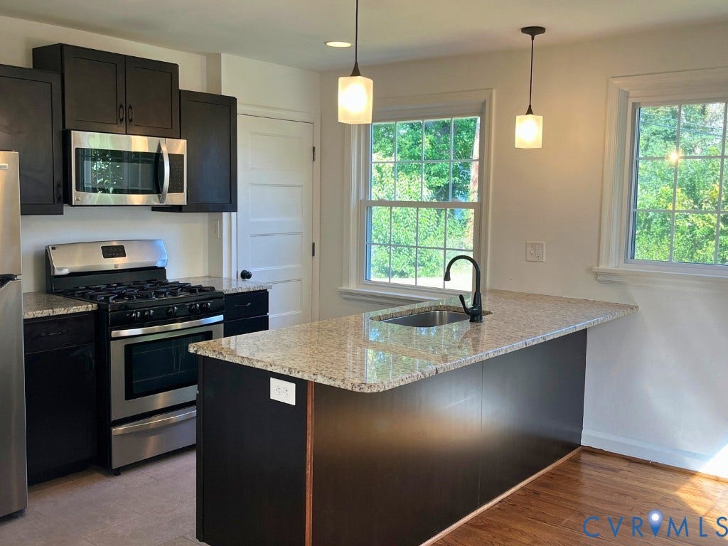 Kitchen featuring dark cabinetry, stone countertops, stainless steel gas range, integrated island with sink, and pendant lighting