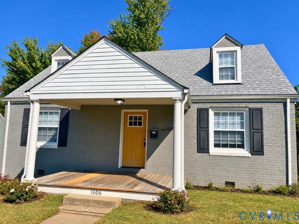 Painted brick exterior featuring a covered front porch with round columns, dormer windows, and a wood-plank porch deck