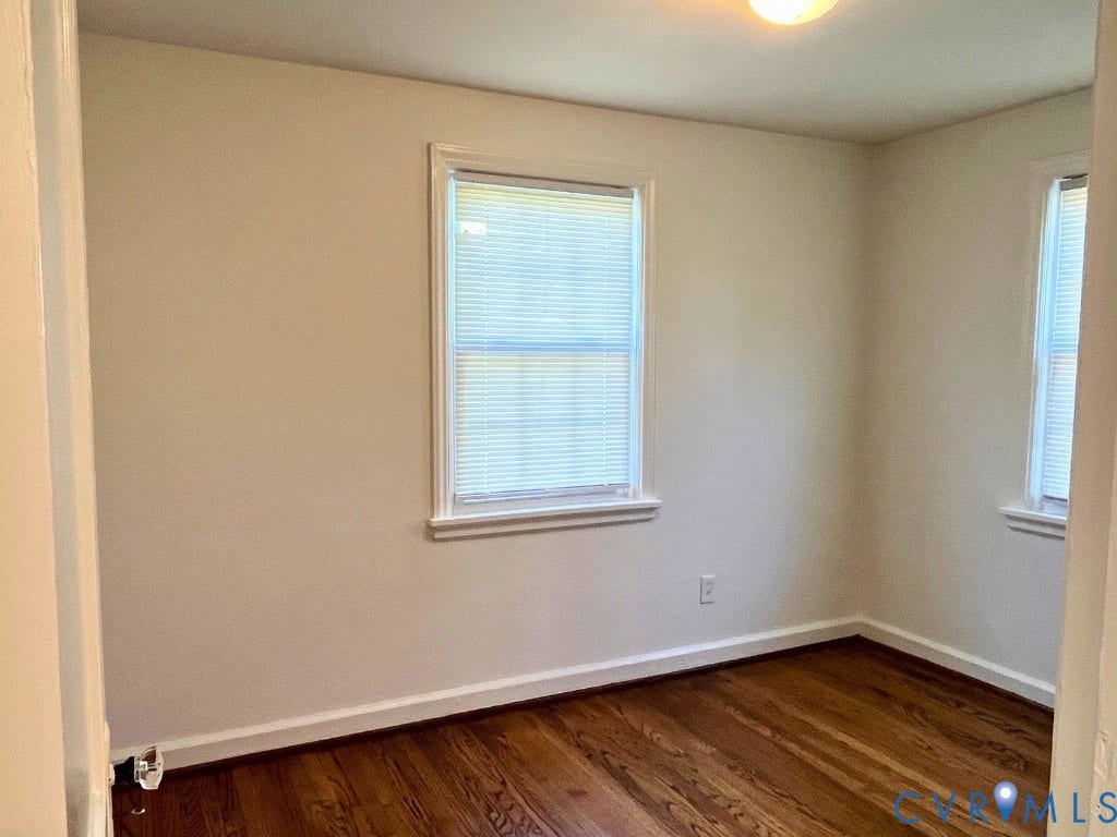 Room featuring wood-finish flooring, neutral-toned wall paint, and dual windows with window blinds