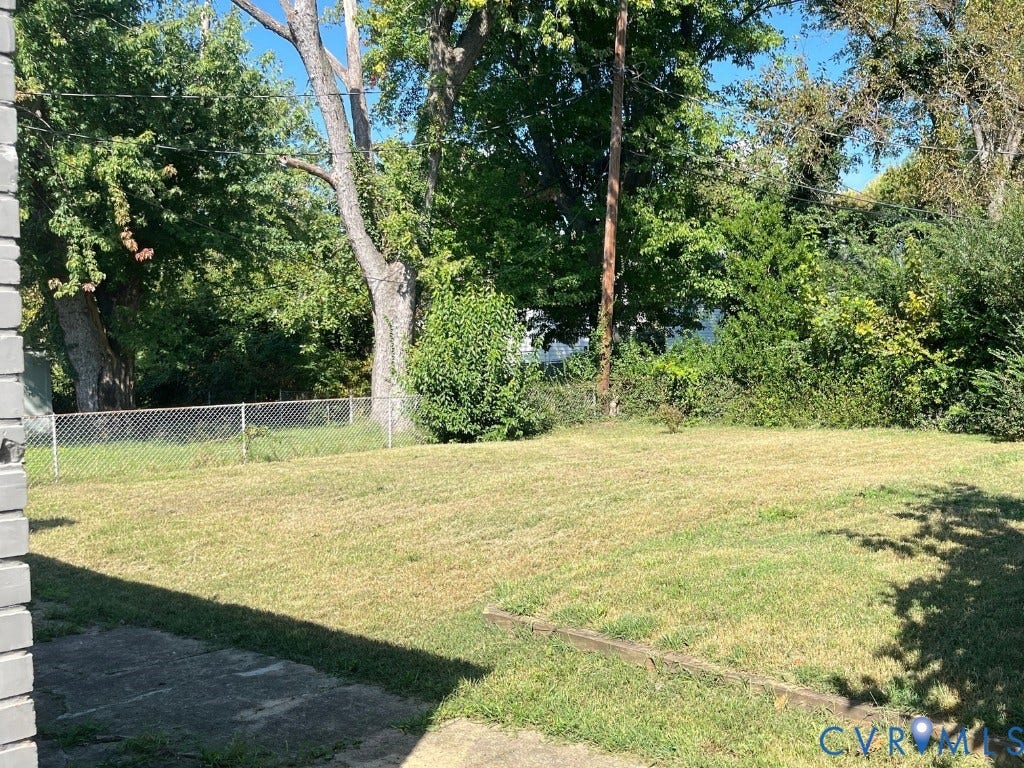 Rear yard featuring a grass lawn, metal chain-link fencing, and mature trees