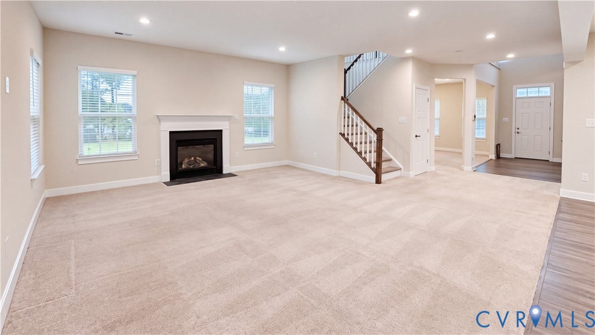11500 Amara Drive, Chesterfield, VA 23838 Open-concept interior featuring a fireplace with a white mantel, recessed lighting, carpeted flooring, and a staircase with a wooden handrail