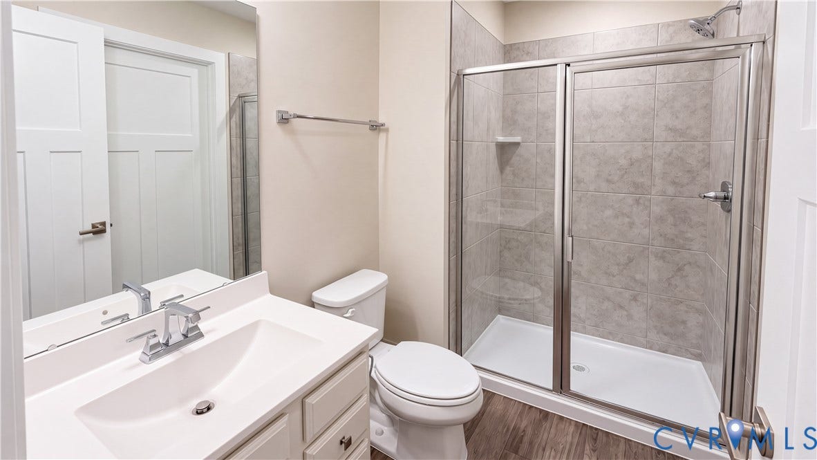 11500 Amara Drive, Chesterfield, VA 23838 Bathroom featuring a vanity with a white countertop and integrated sink, a glass-enclosed shower with tile surround, wood-finish flooring, and a wall-mounted mirror