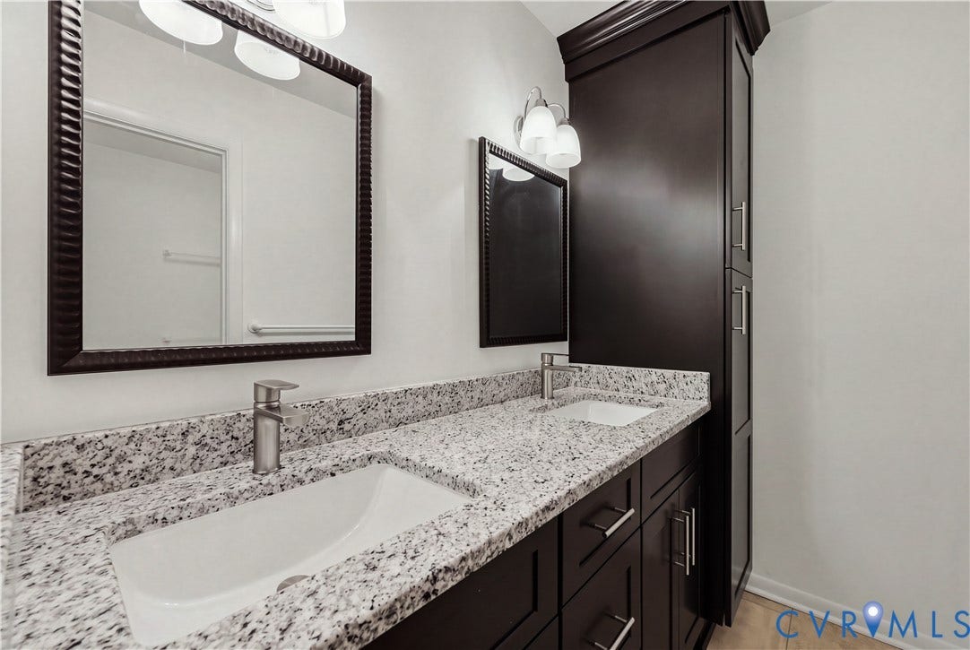 11947 W Briar Patch Drive, Chesterfield, VA 23113 Double vanity featuring dark wood-finish cabinetry, a stone-composite countertop, dual undermount sinks, and integrated floor-to-ceiling storage cabinetry