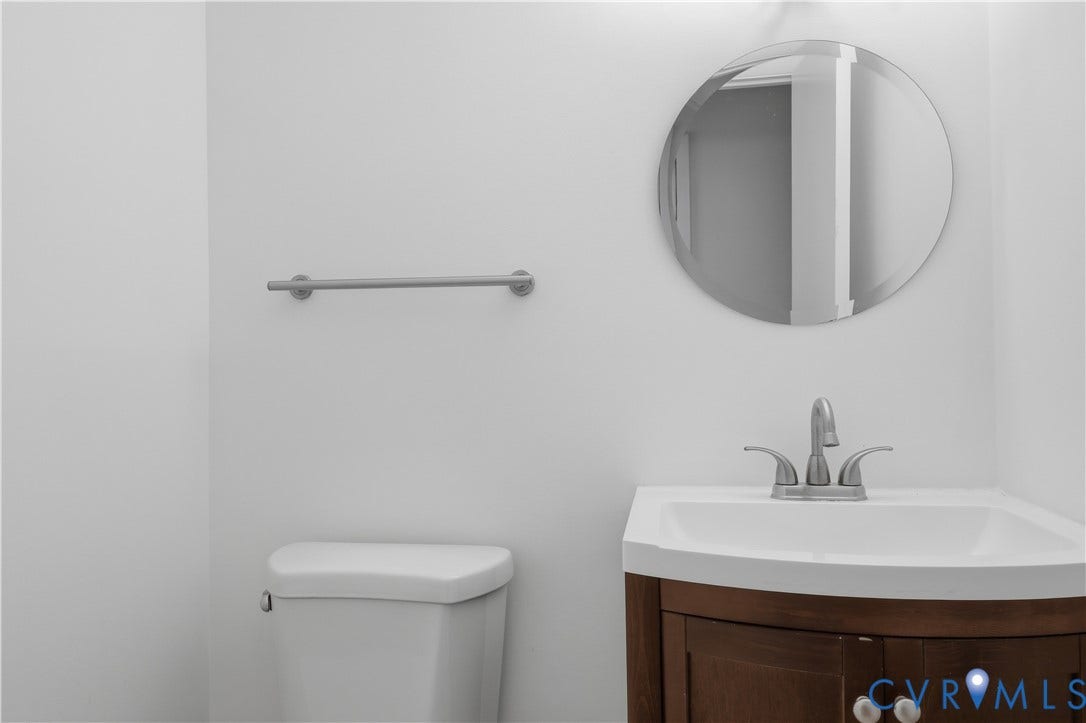 11947 W Briar Patch Drive, Chesterfield, VA 23113 Bathroom featuring a wood-finish vanity with a white integrated basin, a polished metal faucet, a circular wall-mounted mirror, and a metal towel bar