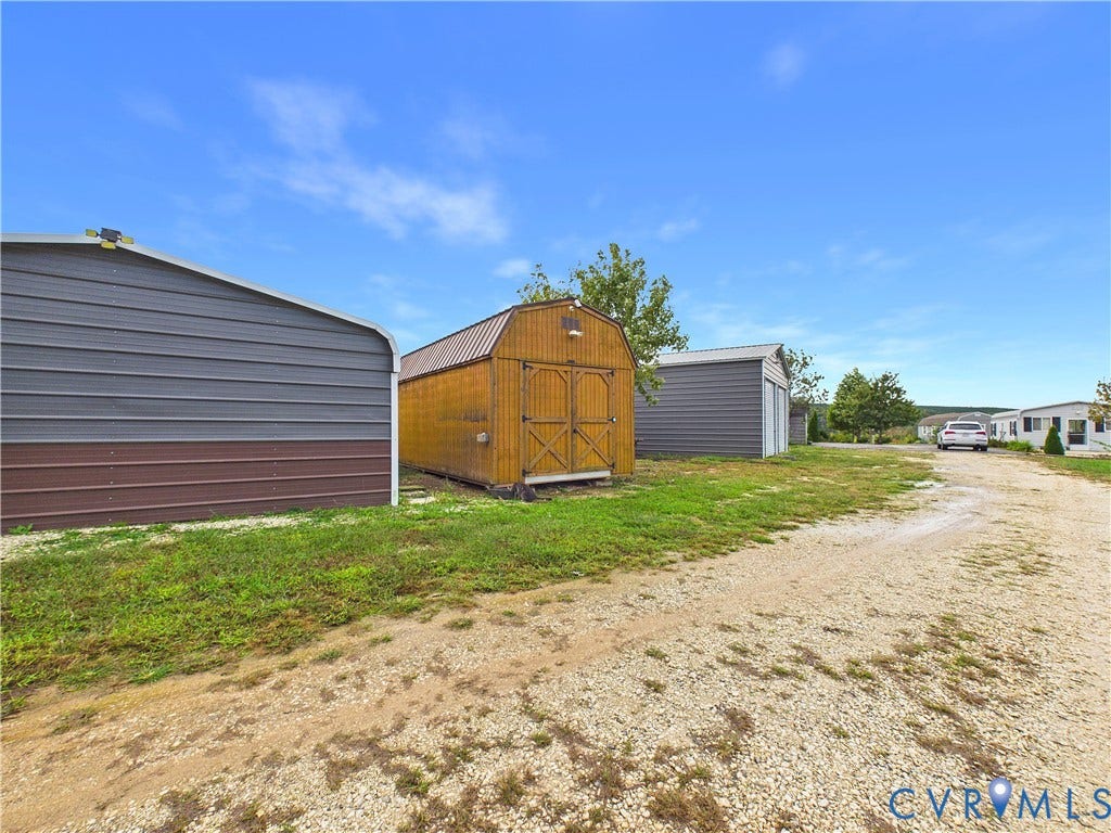 290 Western Lane, Appomattox, Appomattox, VA 24522 Exterior storage structures featuring two metal-sided buildings and a central wood-sided outbuilding with dual doors, situated on a gravel driveway