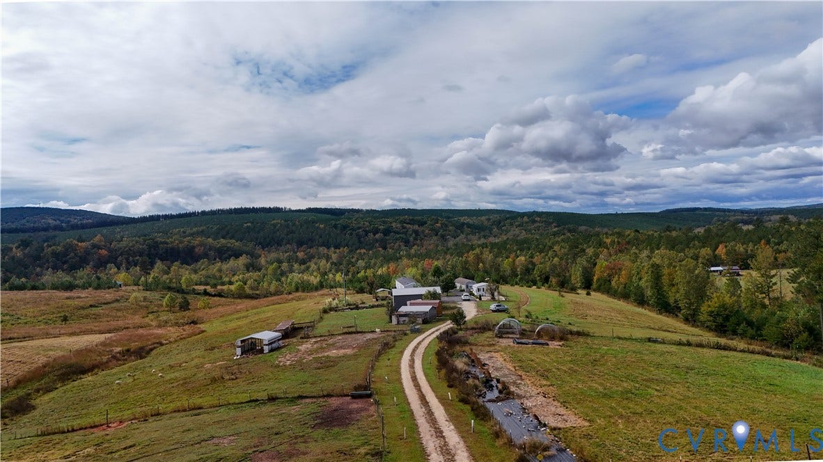 290 Western Lane, Appomattox, Appomattox, VA 24522 Expansive acreage featuring rolling grassy fields, multiple outbuildings, a winding gravel driveway, and a natural creek, set against a backdrop of mature woodland and distant mountain ranges