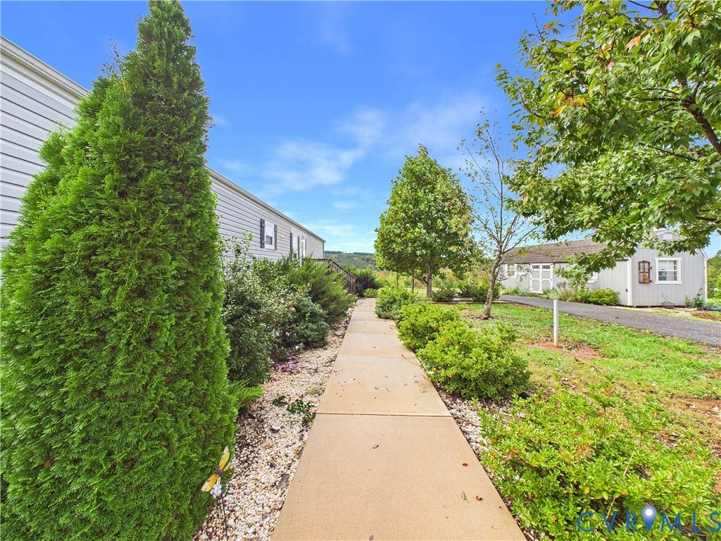 290 Western Lane, Appomattox, Appomattox, VA 24522 Concrete walkway bordered by mature evergreen shrubs, landscaped beds with stone ground cover, and a detached structure with a gravel path