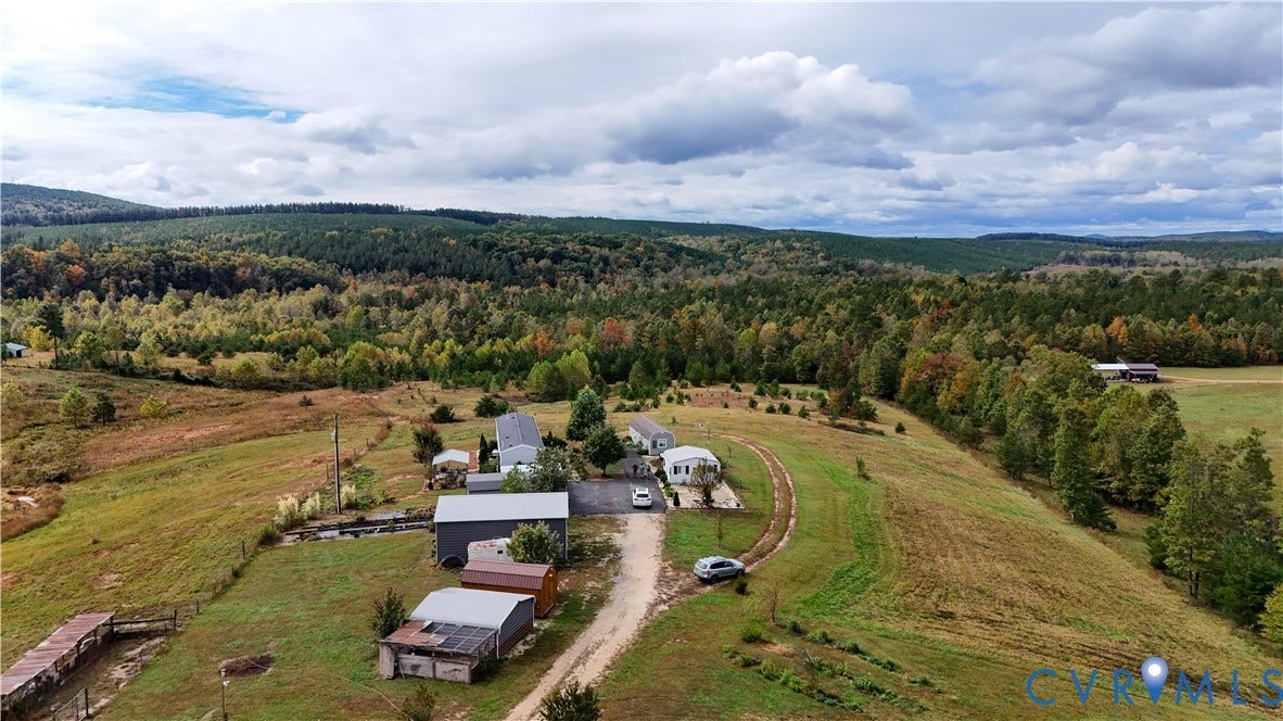 290 Western Lane, Appomattox, Appomattox, VA 24522 Expansive acreage featuring multiple outbuildings, open pasture land, and a gravel driveway set against a forested mountain backdrop