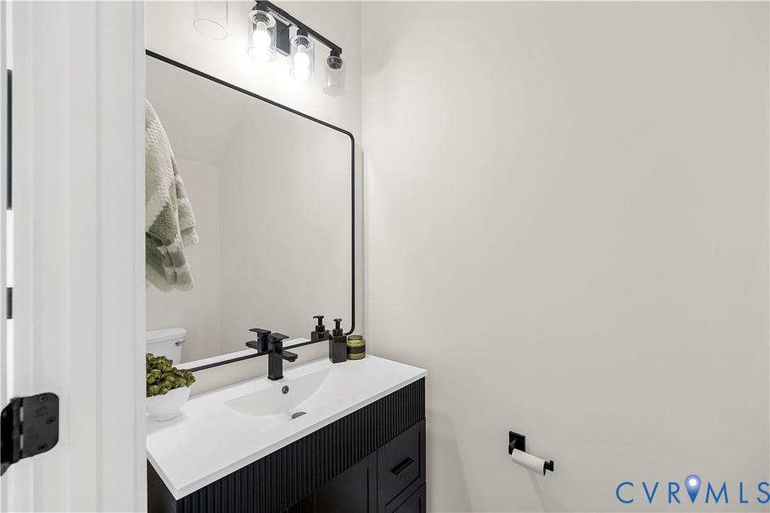 851 E Bank Street, Old Towne, Petersburg, VA 23803 Black fluted vanity with a white countertop, rectangular integrated sink, matte black widespread faucet, and matching black-framed wall mirror with a multi-light fixture