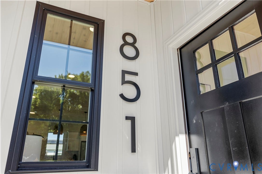 851 E Bank Street, Old Towne, Petersburg, VA 23803 White vertical siding exterior featuring a black entry door with multi-pane glass inserts, dark-framed window, and matte black oversized house numbers