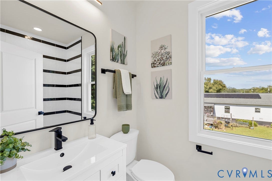 851 E Bank Street, Old Towne, Petersburg, VA 23803 White vanity with a rectangular sink, matte black faucet, wall-mounted mirror with a black frame, and shower enclosure featuring horizontal black and white tile accents