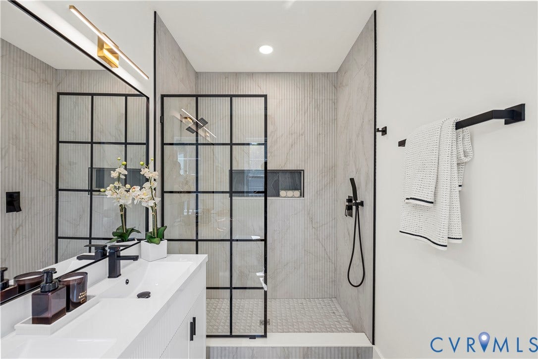 851 E Bank Street, Old Towne, Petersburg, VA 23803 Walk-in shower featuring a grid-patterned black frame glass enclosure, floor-to-ceiling textured tile wall, recessed niche, and matte black handheld shower fixture, complemented by a dual-sink vanity with matte black hardware