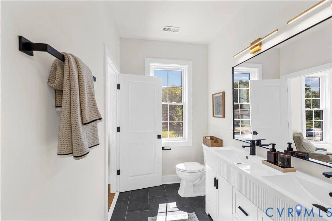 851 E Bank Street, Old Towne, Petersburg, VA 23803 Bathroom featuring a white dual-sink vanity with fluted cabinetry, large rectangular mirrors, matte black fixtures, and dark-toned floor tiling
