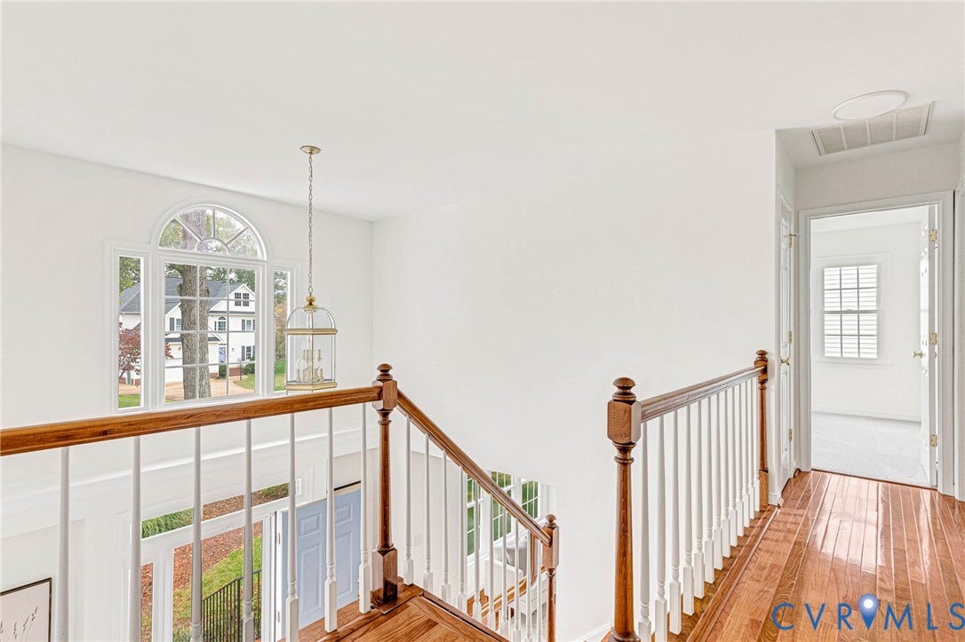3629 Milbury Run Street, Henrico, VA 23233 Landing featuring wood-finish flooring, a traditional staircase with a wooden handrail, white spindle balusters, a decorative hanging pendant light, and an arched window