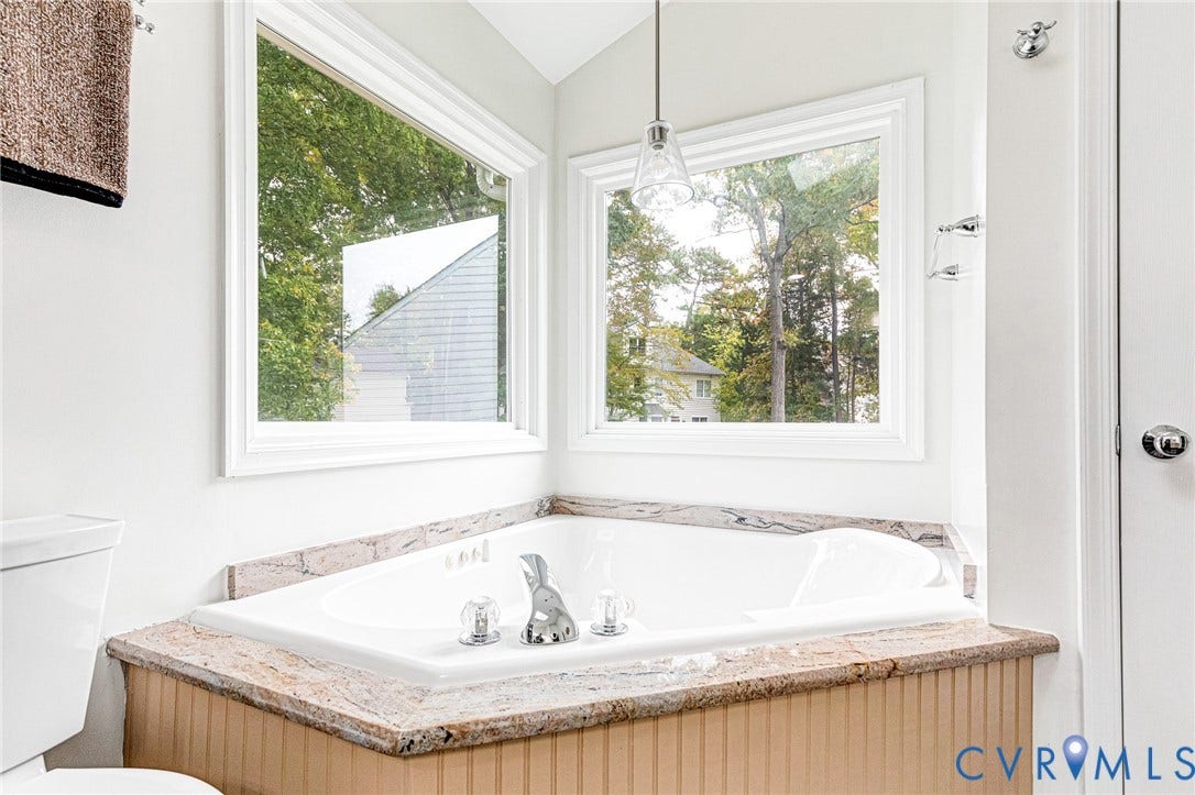 3629 Milbury Run Street, Henrico, VA 23233 Corner soaking tub featuring a stone-surface surround, beadboard paneling, chrome fixtures, and dual picture windows with pendant lighting