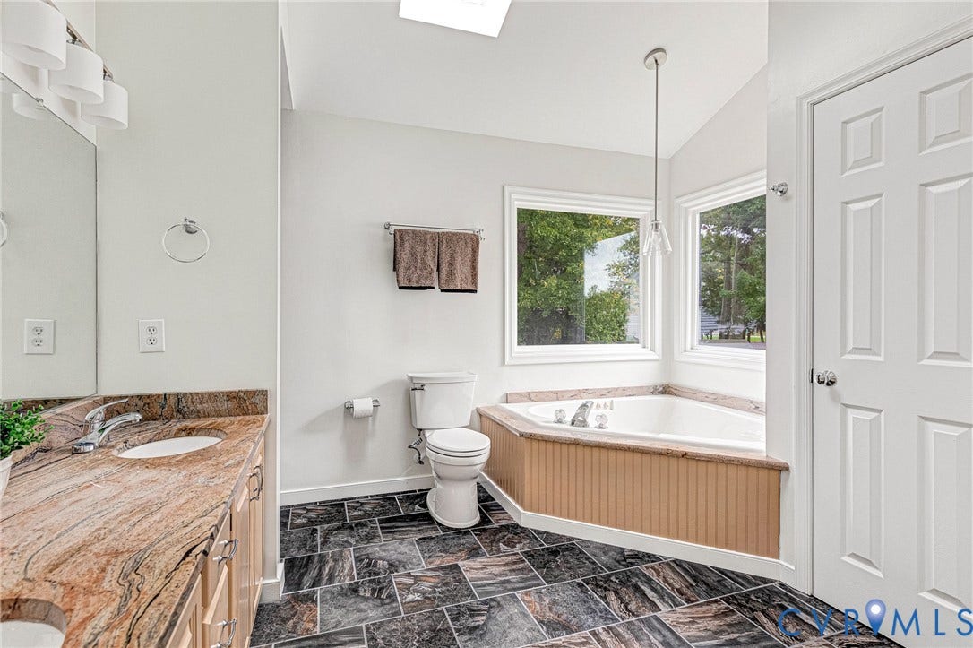 3629 Milbury Run Street, Henrico, VA 23233 Stone countertop vanity, large soaking tub with tile surround, vaulted ceiling with skylight, and stone-finish floor tile