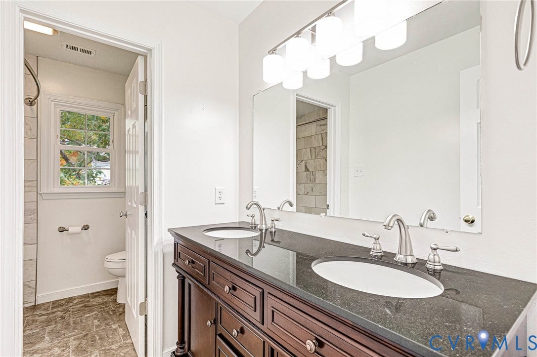3629 Milbury Run Street, Henrico, VA 23233 Double vanity featuring a dark stone countertop, dual undermount sinks, wood-finish cabinetry, a large wall-mounted mirror, and multi-bulb vanity lighting