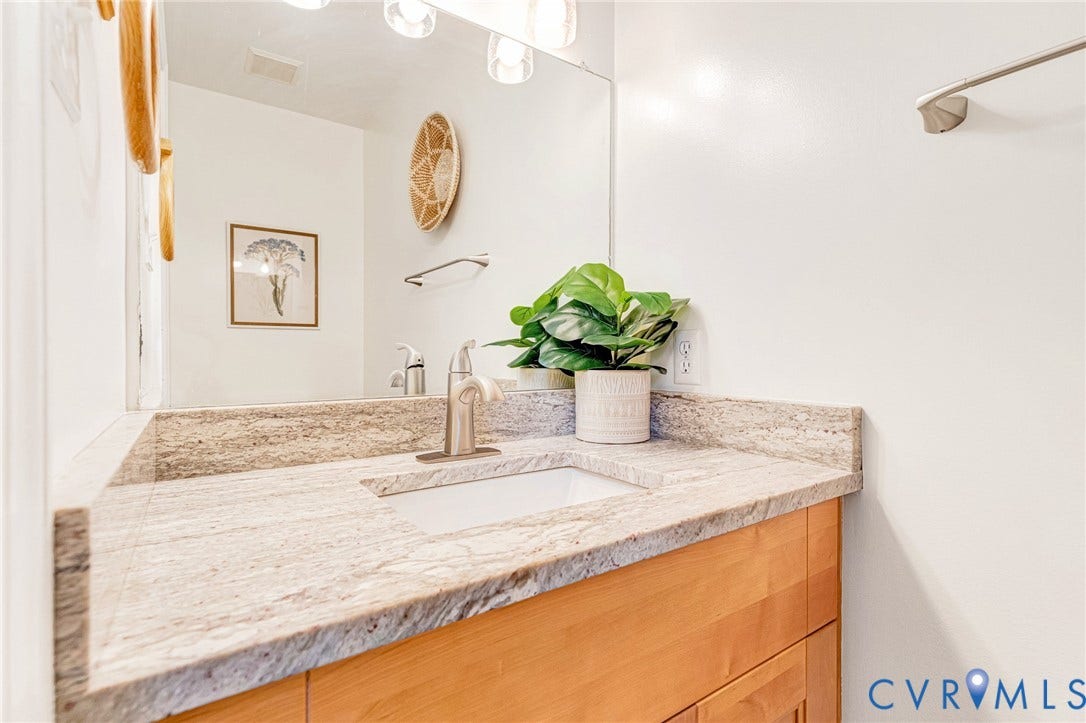 3629 Milbury Run Street, Henrico, VA 23233 Vanity featuring a stone-surface countertop, an integrated rectangular undermount sink, a brushed-metal single-handle faucet, light-finish wooden cabinetry, and a full-width wall-mounted mirror