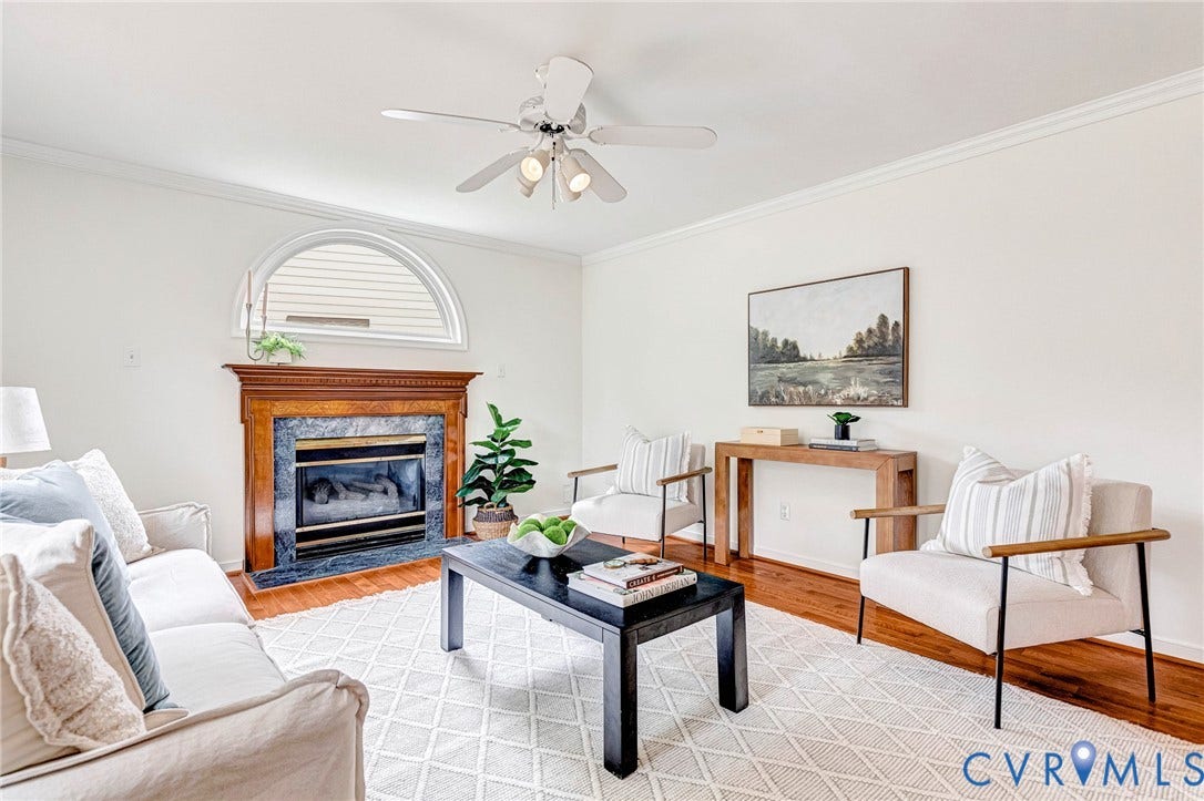 3629 Milbury Run Street, Henrico, VA 23233 Fireplace featuring a decorative wood mantel, stone surround, and an arched transom window above, complemented by wood-finish flooring and a central ceiling fan with integrated lighting