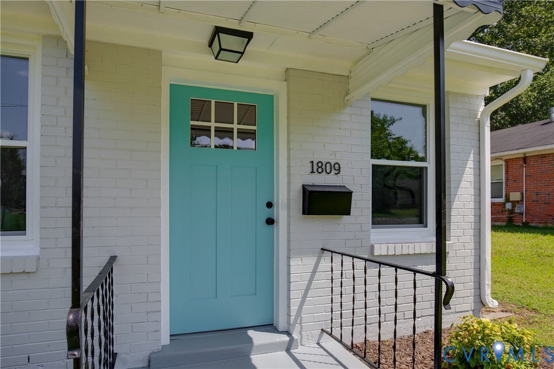 1809 Sussex Street, Whitcomb, Richmond, VA 23223 Painted brick exterior featuring a teal-accented front door with glass insert, black wrought-iron porch railings, and a geometric flush-mount light fixture