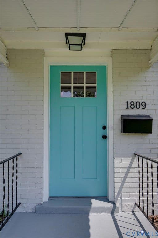 1809 Sussex Street, Whitcomb, Richmond, VA 23223 Painted brick exterior entry featuring a paneled door with a six-pane window, black metal hardware, a wall-mounted mailbox, and a recessed ceiling light fixture