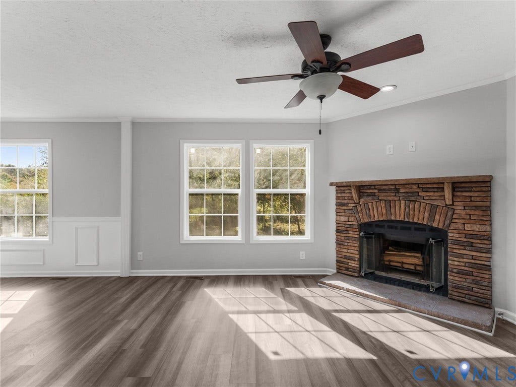 1625 Cedar Lane, Powhatan, VA 23139 Stone-facade fireplace with a wooden mantel, wood-finish flooring, multi-pane windows, grid-pattern wall molding, and a ceiling fan with integrated lighting