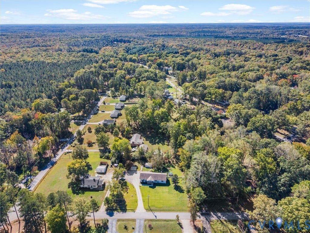 1625 Cedar Lane, Powhatan, VA 23139 Aerial perspective of a multi-acre property featuring expansive grassy clearings, mature hardwood timber, and paved driveway access