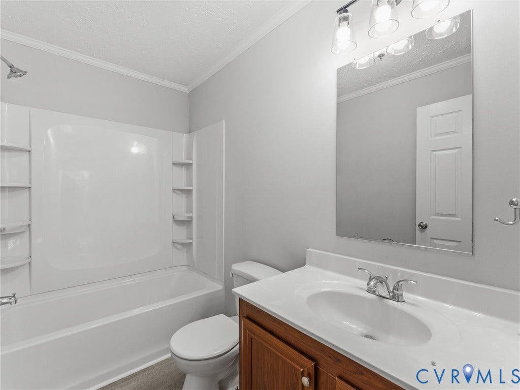 1625 Cedar Lane, Powhatan, VA 23139 Bathroom featuring a wood-finish vanity with a composite countertop, integrated oval basin, polished chrome faucet, multi-light fixture, and a tub-shower combination with built-in shelving