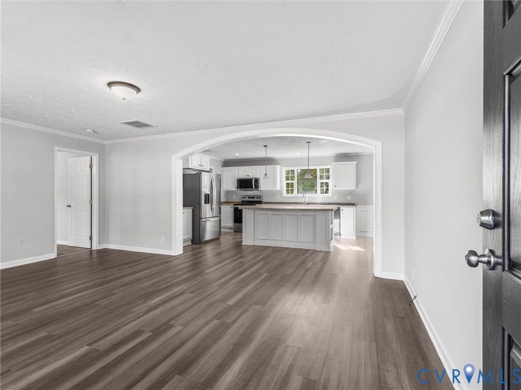 1625 Cedar Lane, Powhatan, VA 23139 Open floor plan featuring a prominent architectural archway, wood-finish flooring, white cabinetry, a kitchen island, and stainless steel appliances